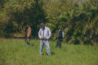 Three young men in formal attire stand outdoors in a grassy area in Accra, Ghana, showcasing modern fashion.