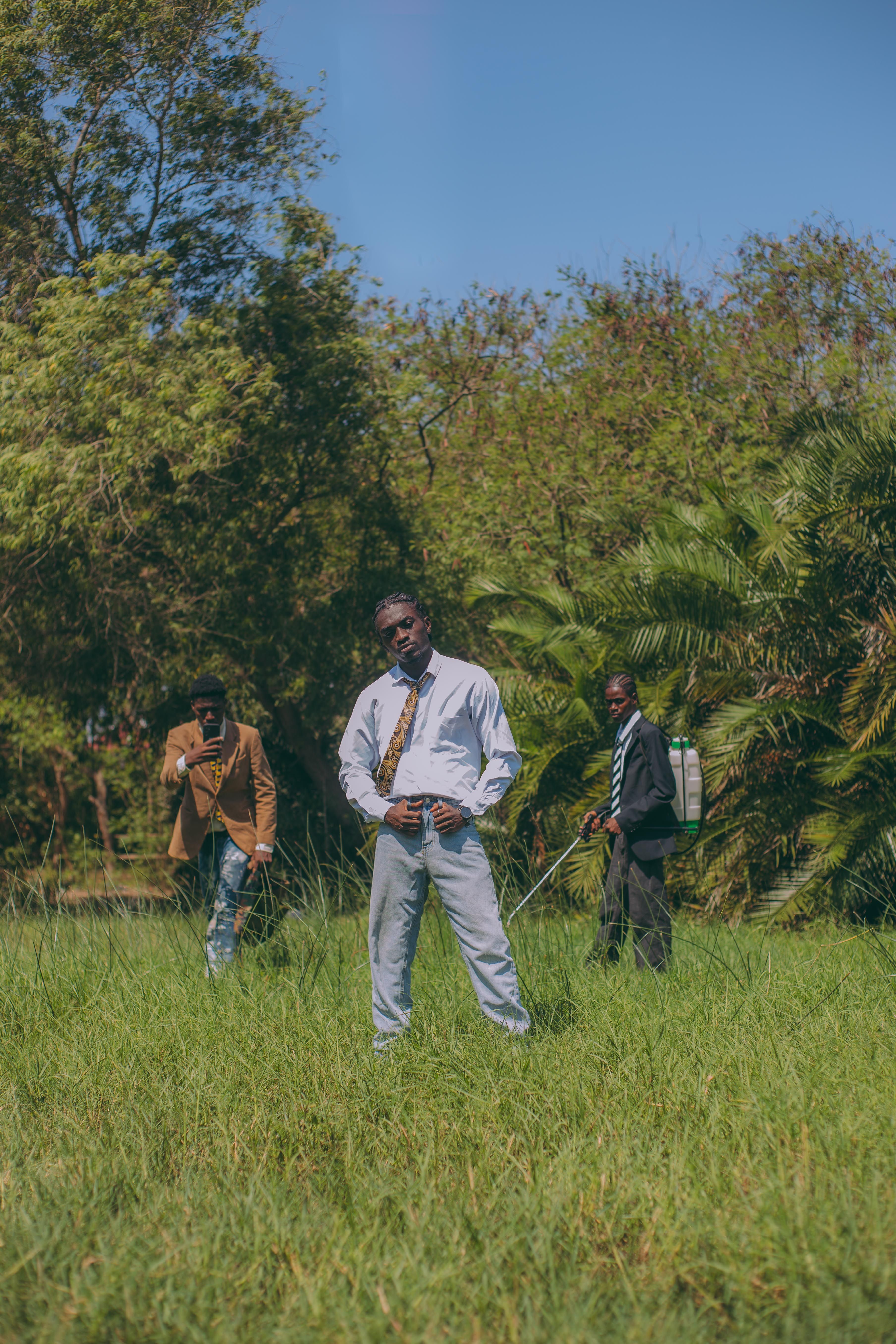 Three fashionable men stand confidently in an outdoor setting surrounded by vibrant greenery.