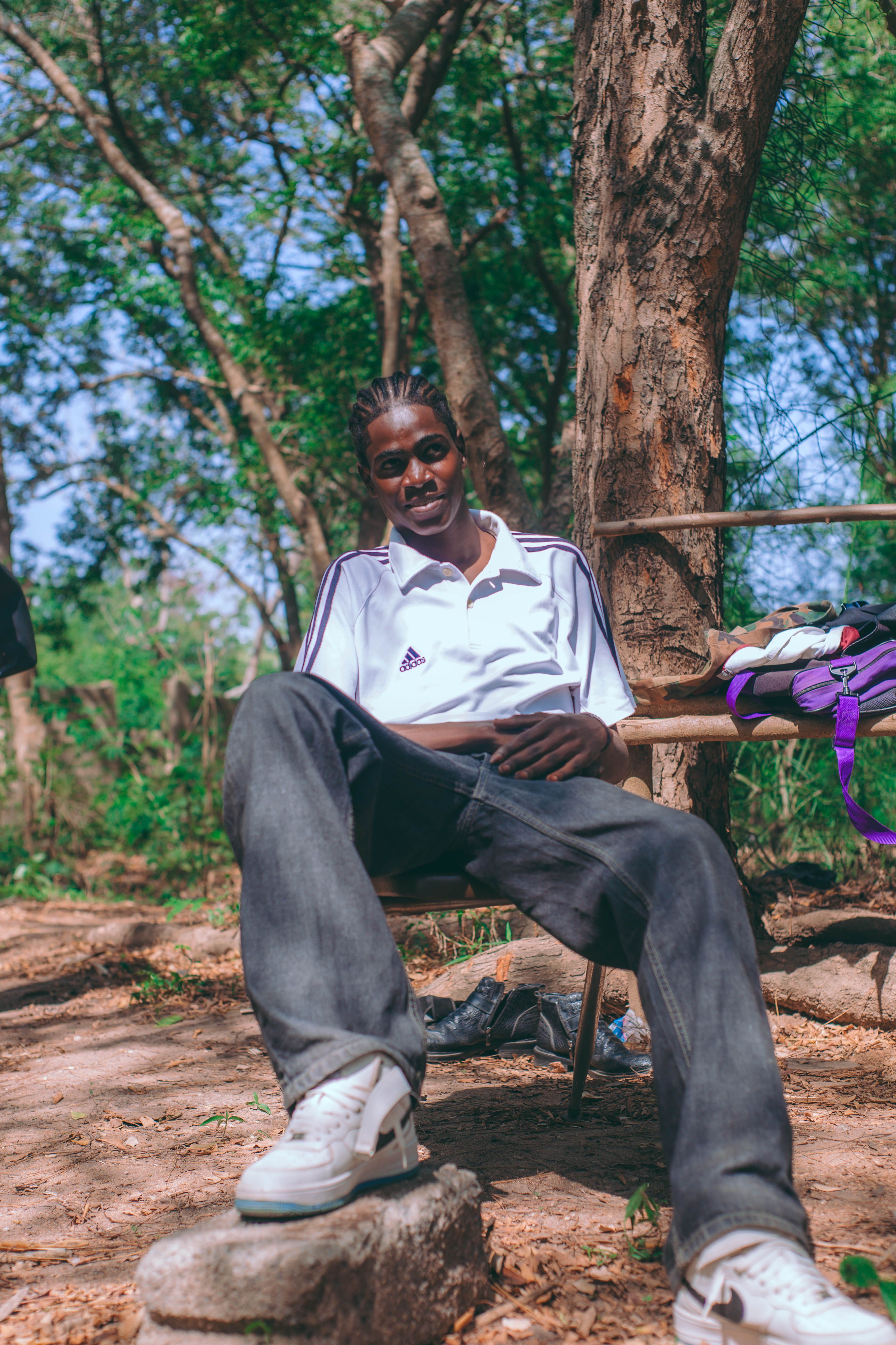 Casual young man seated outdoors in a natural setting, enjoying a sunny day.