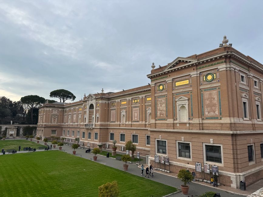Wide view of the Vatican Museums showcasing classical architecture with a manicured lawn.