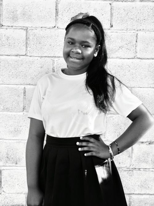 Free Monochrome portrait of a confident teenage girl posing with a smile against a brick wall, showcasing youthful elegance. Stock Photo