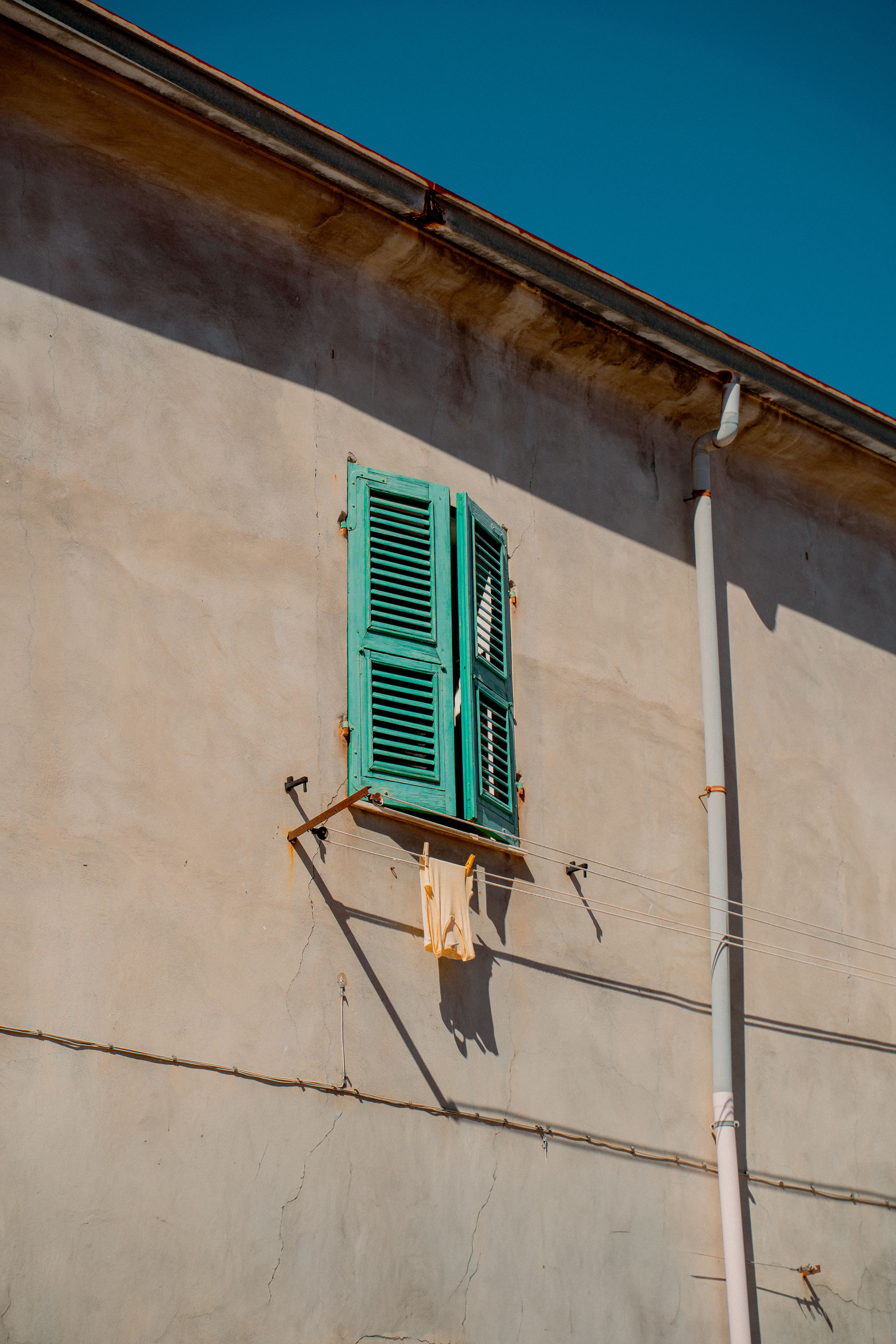 A charming rustic wall with turquoise shutters in Sardegna, Italy, under clear skies.