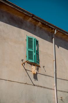 A charming rustic wall with turquoise shutters in Sardegna, Italy, under clear skies.