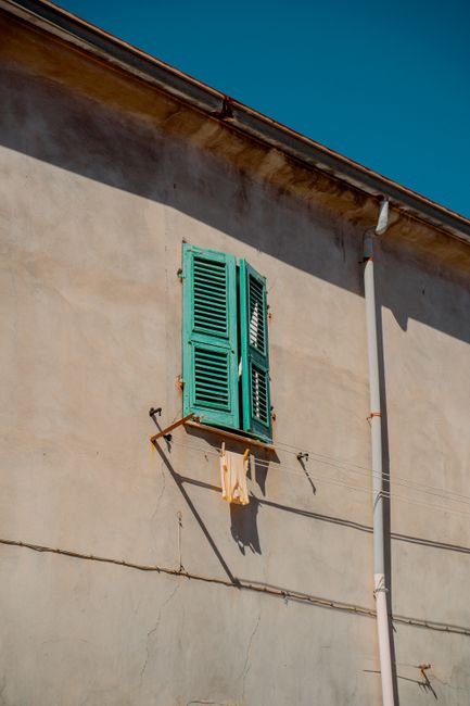 A charming rustic wall with turquoise shutters in Sardegna, Italy, under clear skies.