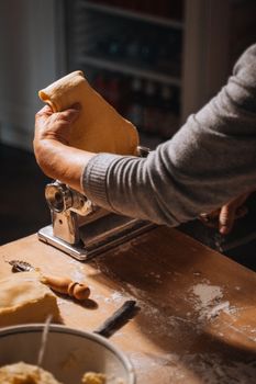 Artisan hands rolling dough through a pasta machine in a warm Italian kitchen.