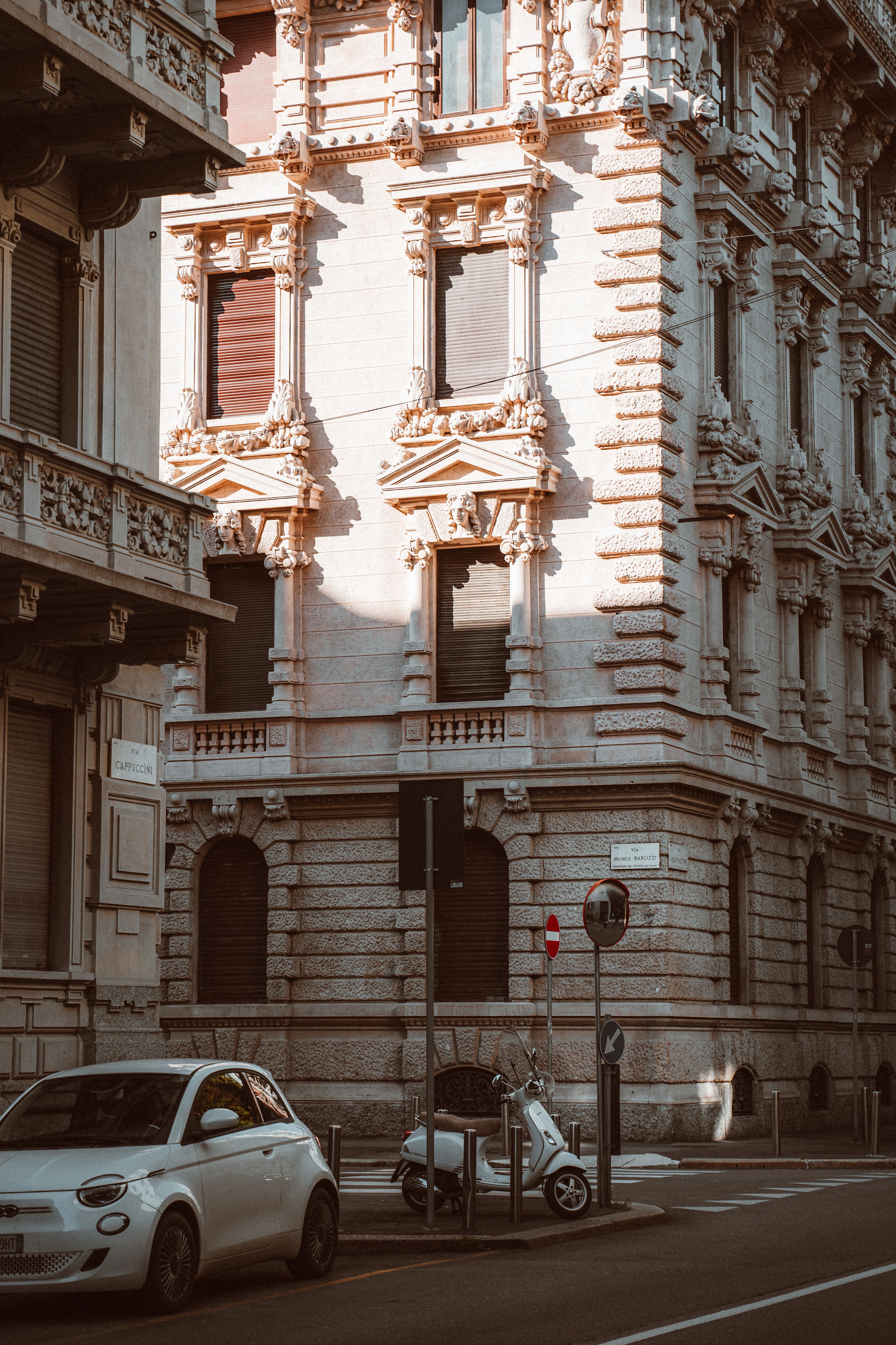 Classic architecture showcasing a historic ornate building facade in Milan, Italy, with parked vehicles on a city street.