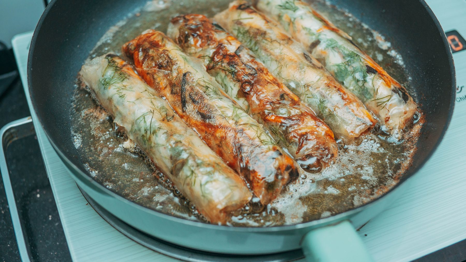 Delicious fried spring rolls sizzling in a pan over a stove, crispy and golden brown.