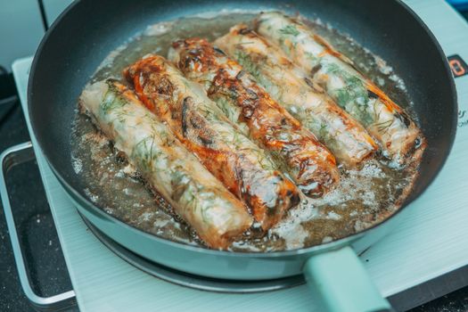 Delicious fried spring rolls sizzling in a pan over a stove, crispy and golden brown.