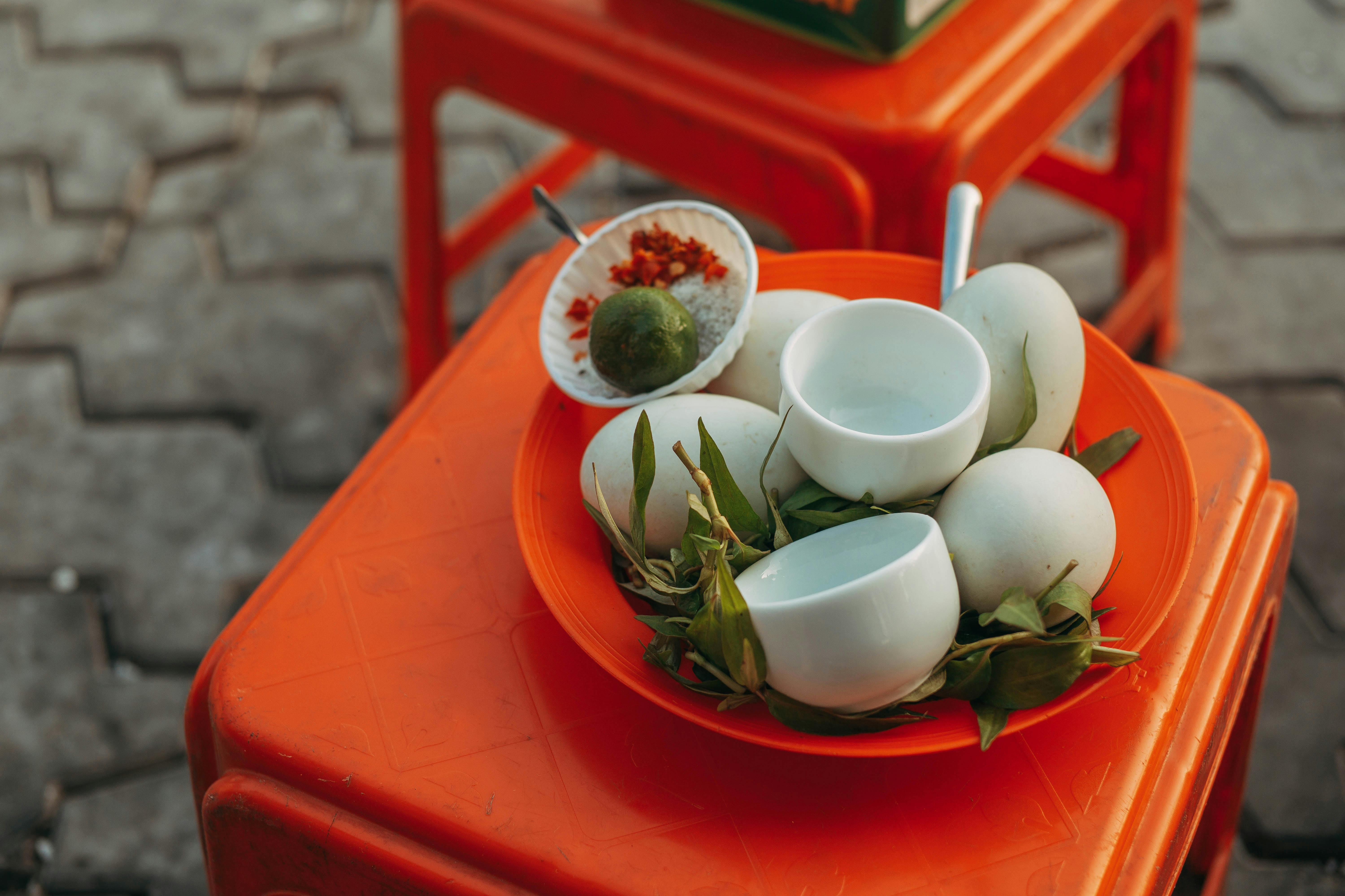 Close-up of a traditional street food setup featuring duck eggs, herbs, lime, and spices on an orange stool.