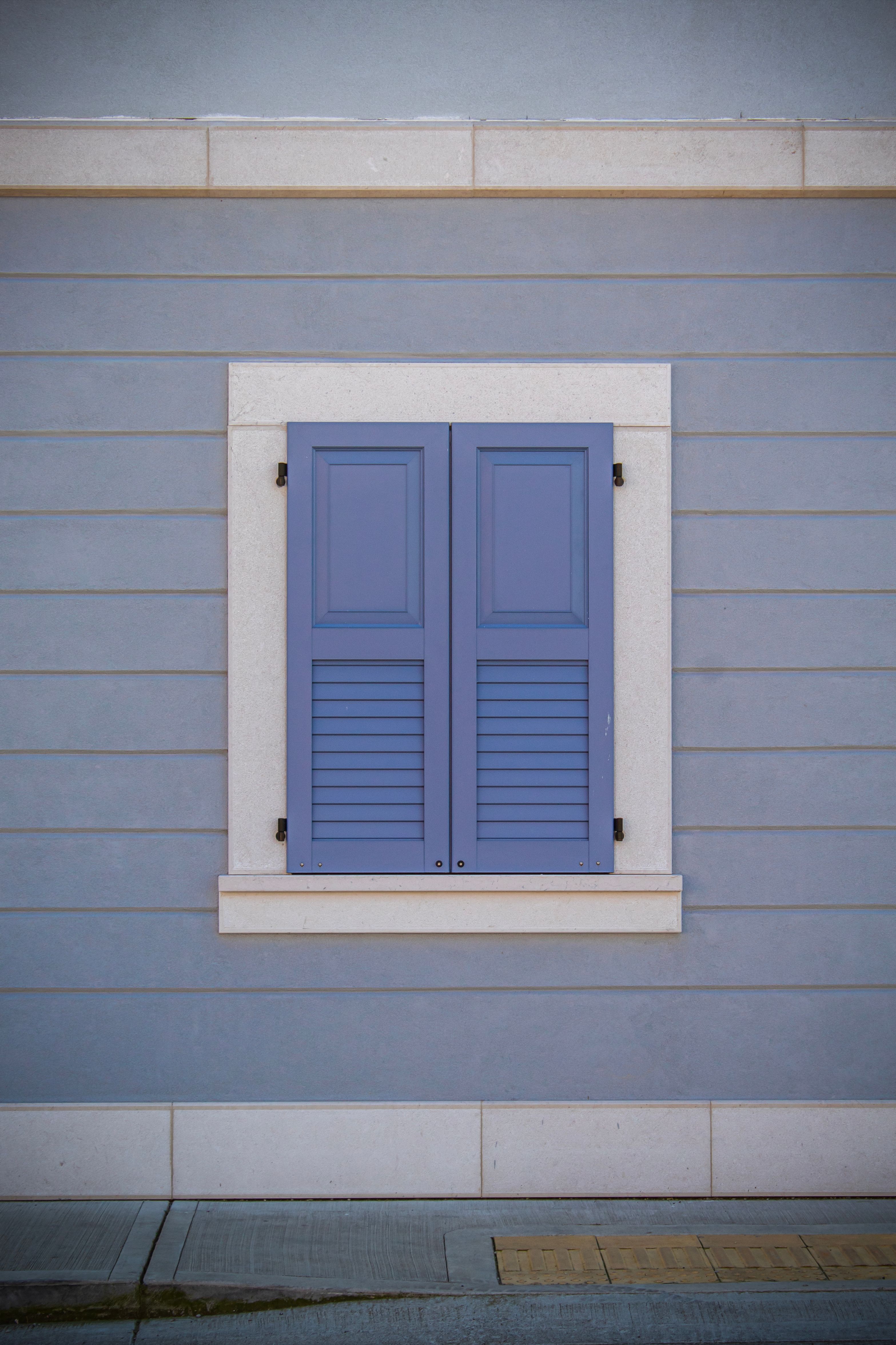 A picturesque blue shuttered window on a pastel wall in Palmanova, Italy.