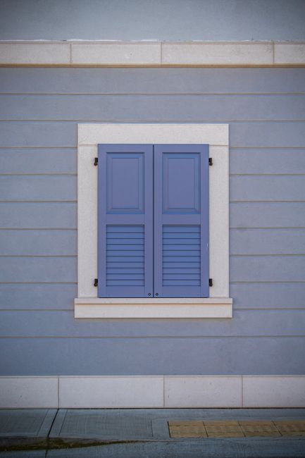 A picturesque blue shuttered window on a pastel wall in Palmanova, Italy.