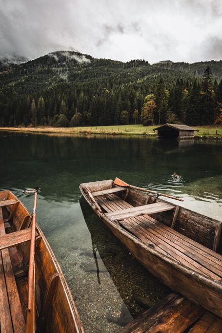 Scenic view of wooden rowboats on a serene mountain lake surrounded by lush forest.