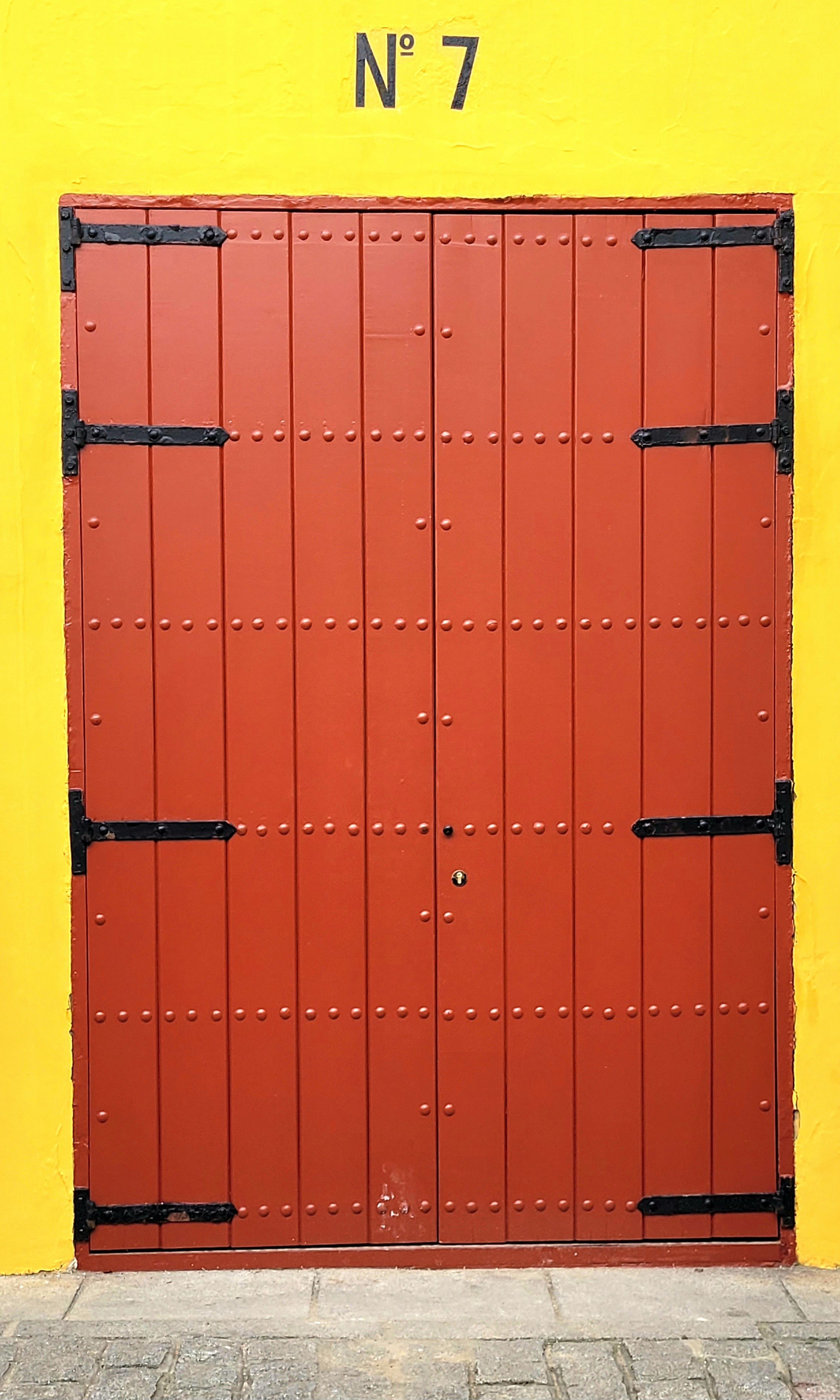 A rustic red wooden door set against a vibrant yellow wall with 'No. 7' above, offering a striking contrast.