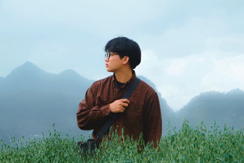 Free A man stands amidst green foliage with misty mountains in the backdrop, creating a serene nature portrait. Stock Photo