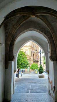 View through an ancient archway revealing a city street with trees and classic architecture.