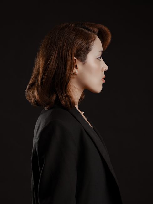 Elegant side profile portrait of a woman wearing a black jacket against a dark background.