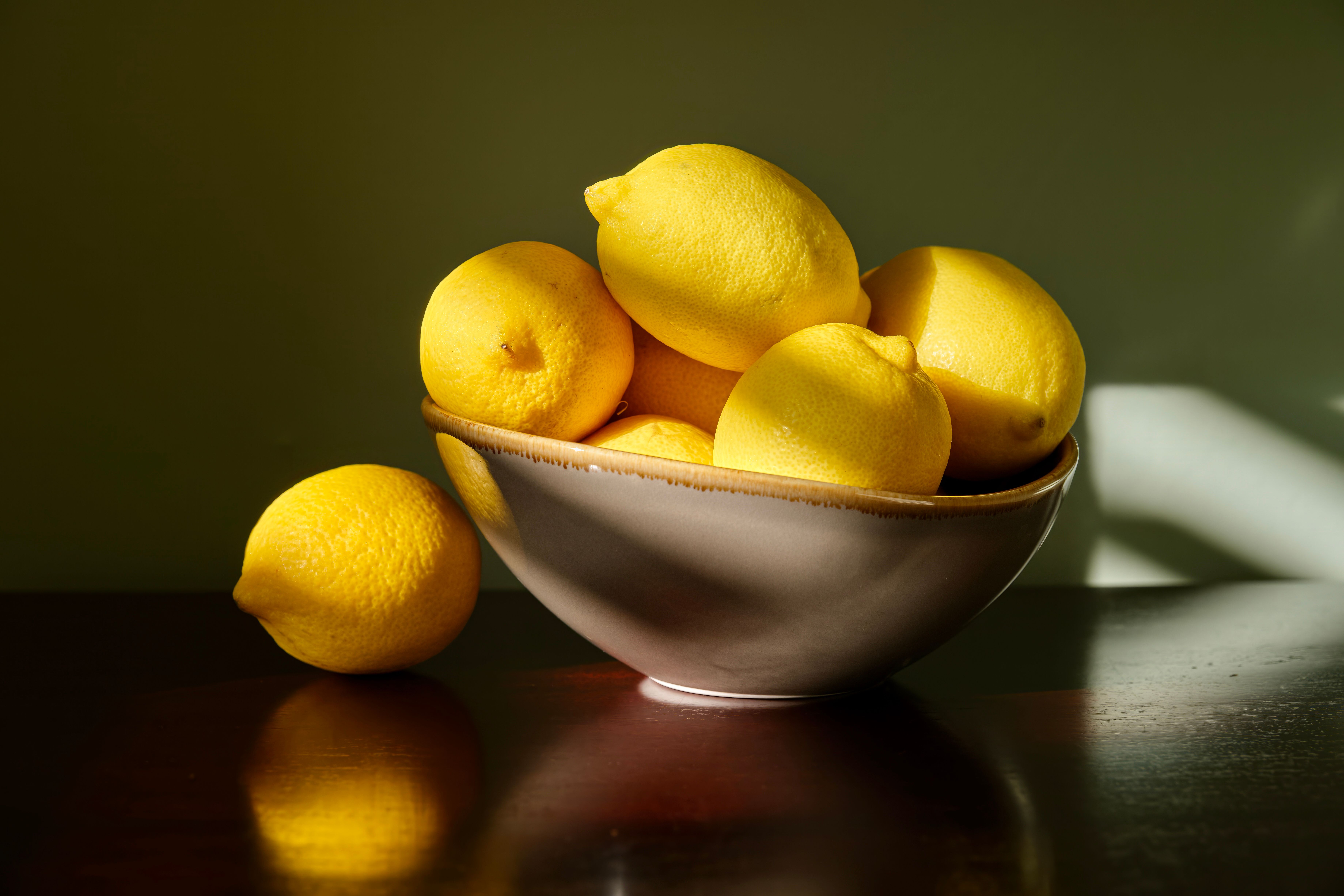 A vibrant arrangement of fresh lemons in a ceramic bowl, bathed in soft morning light, creating an inviting still life.