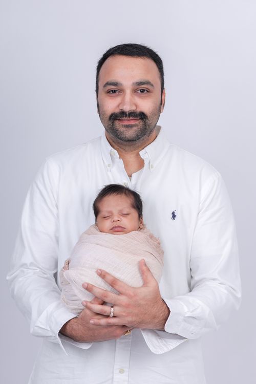 Free Portrait of a father lovingly holding his swaddled newborn baby in a studio setting. Stock Photo