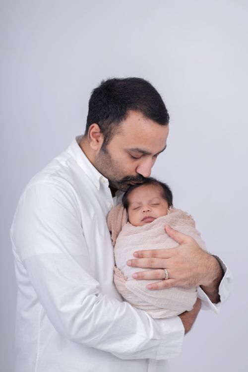 Free Father lovingly holding newborn, conveying warmth and protection against a neutral background. Stock Photo