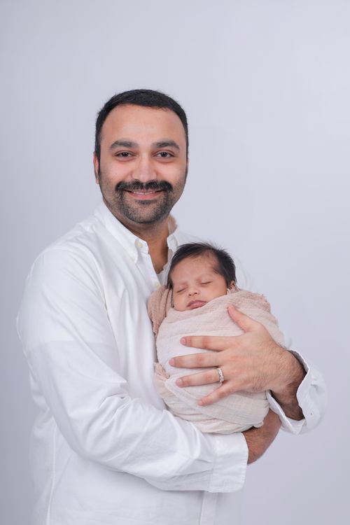 Free A father lovingly holds his newborn baby wrapped in a beige blanket in a studio setting. Stock Photo
