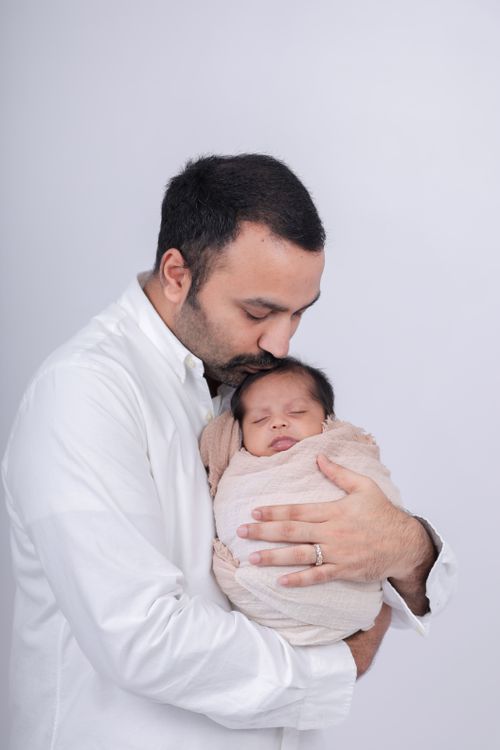 Free A tender moment of a father kissing his newborn baby wrapped in a blanket, set against a soft white background. Stock Photo