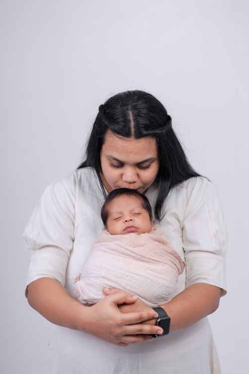 Free Tender moment of mother kissing her newborn, creating a bond of love and warmth in a white studio setting. Stock Photo