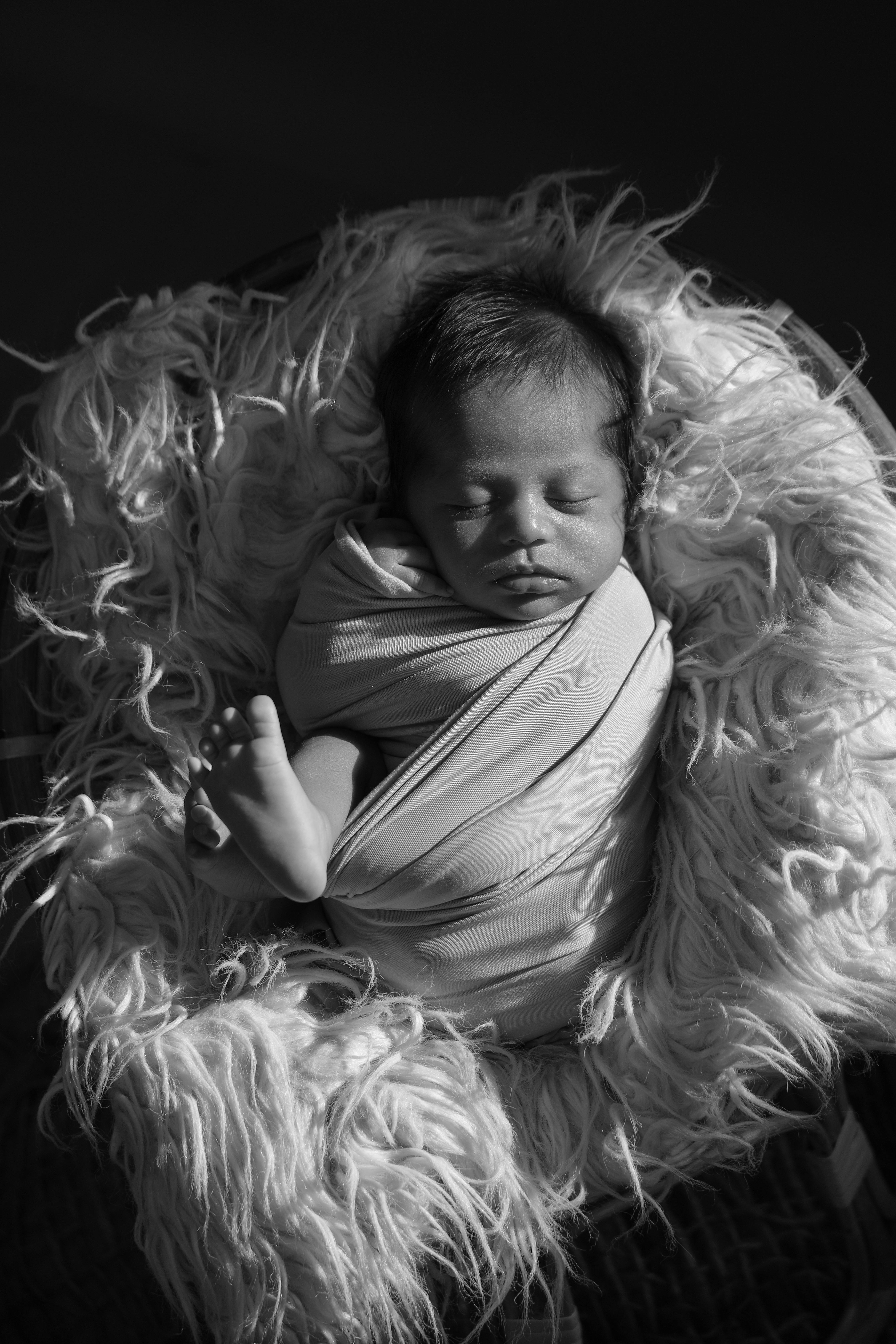 Black and white photo of a newborn baby sleeping peacefully in a cozy wrap.