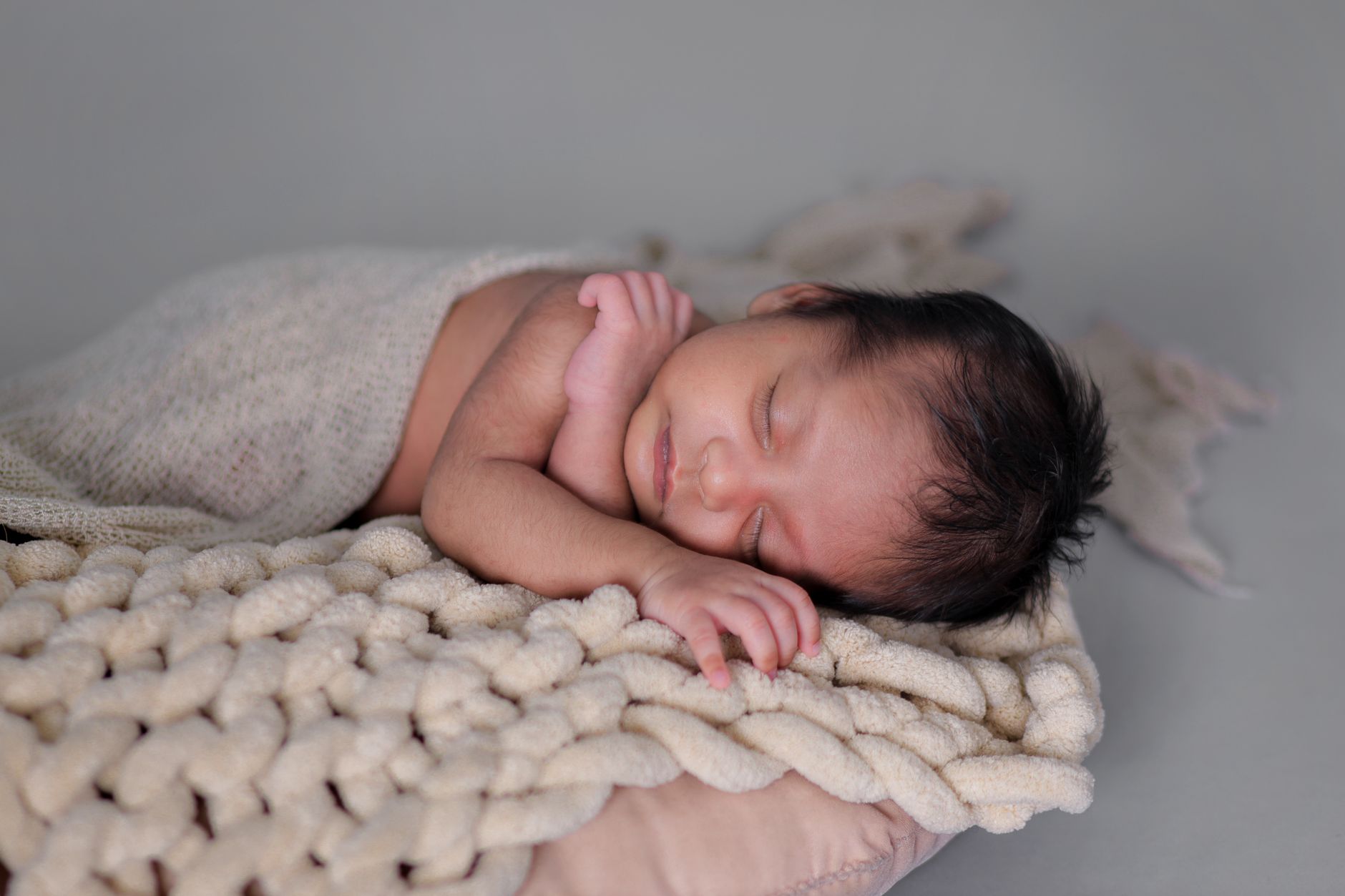 A serene newborn baby peacefully sleeps on a soft knitted blanket, wrapped in a warm fabric.