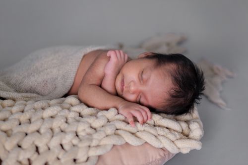 Free A serene newborn baby peacefully sleeps on a soft knitted blanket, wrapped in a warm fabric. Stock Photo