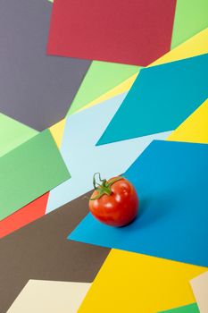 A ripe tomato placed on a colorful geometric paper background, showcasing vibrant hues and artistic composition.