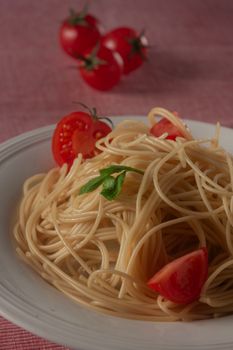 Plate of cooked spaghetti garnished with fresh cherry tomatoes and basil leaves.