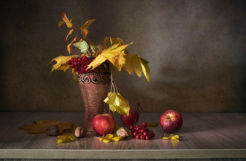 Free A classic still life featuring autumn leaves, apples, and grapes in a vase, evoking fall's warmth and richness. Stock Photo