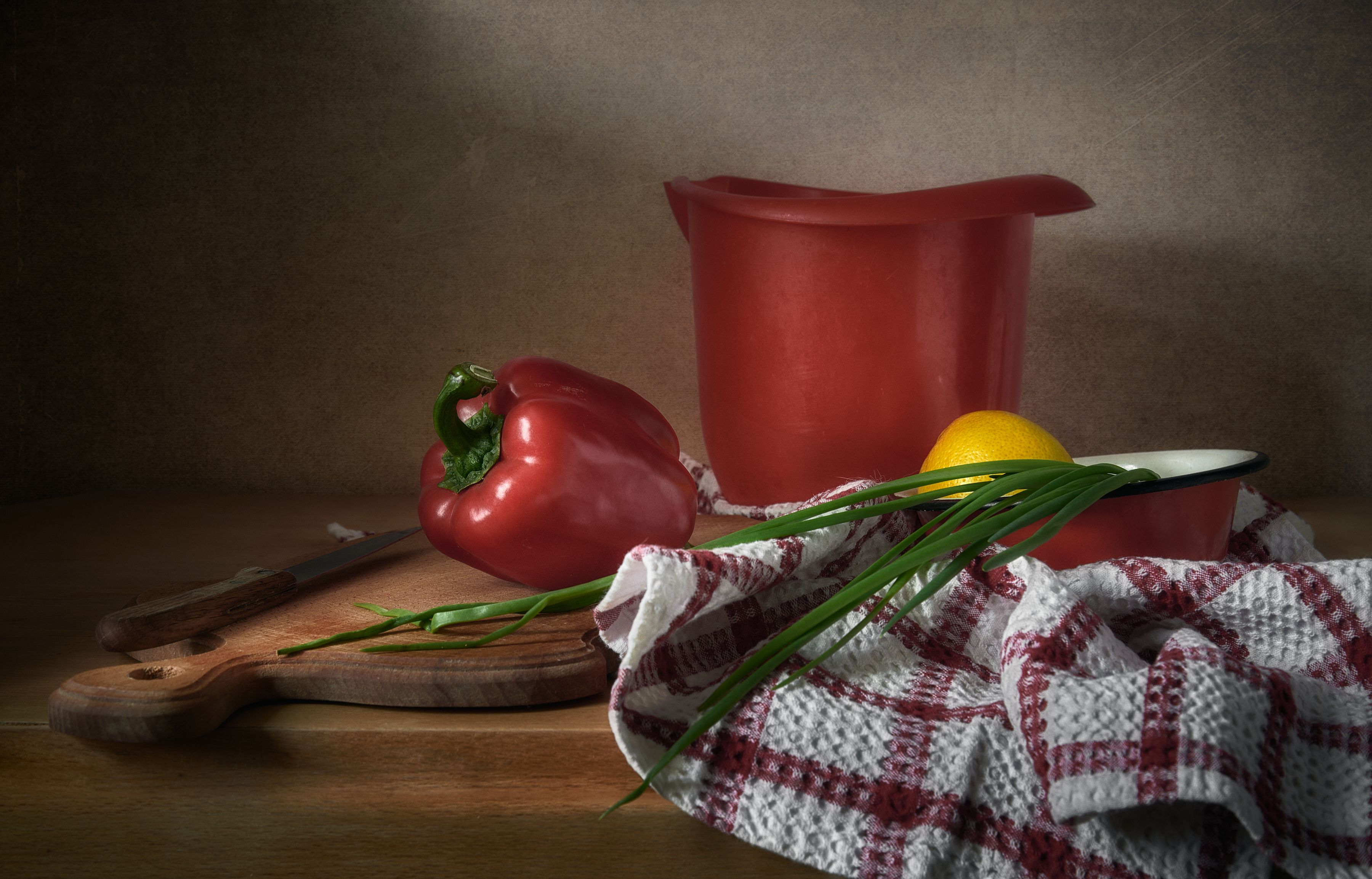 A rustic kitchen setup with red pepper, lemon, and herbs on a wooden board.