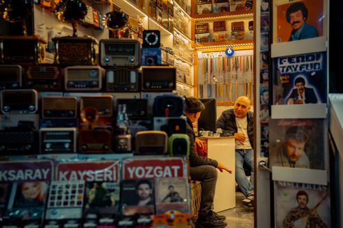 Free A cozy vintage shop filled with old radios and nostalgic posters, featuring two men in conversation. Stock Photo