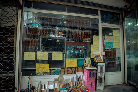 Vibrant display of knives and beads in a Turkish shop. Various signs with prices.