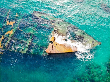 无人机在碧绿而充满活力的海水中，拍摄了一艘被海浪和海洋生物环绕的沉船