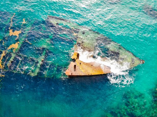 Free Drone shot capturing a sunken shipwreck in vibrant turquoise waters, surrounded by waves and marine life. Stock Photo