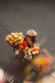 A street vendor in Hanoi, Vietnam, carries a basket of fresh fruits on a bicycle, capturing the essence of local life.