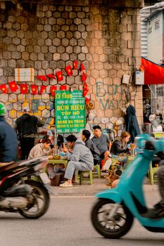 Vibrant Hanoi street life with locals dining by the roadside amid passing motorbikes.