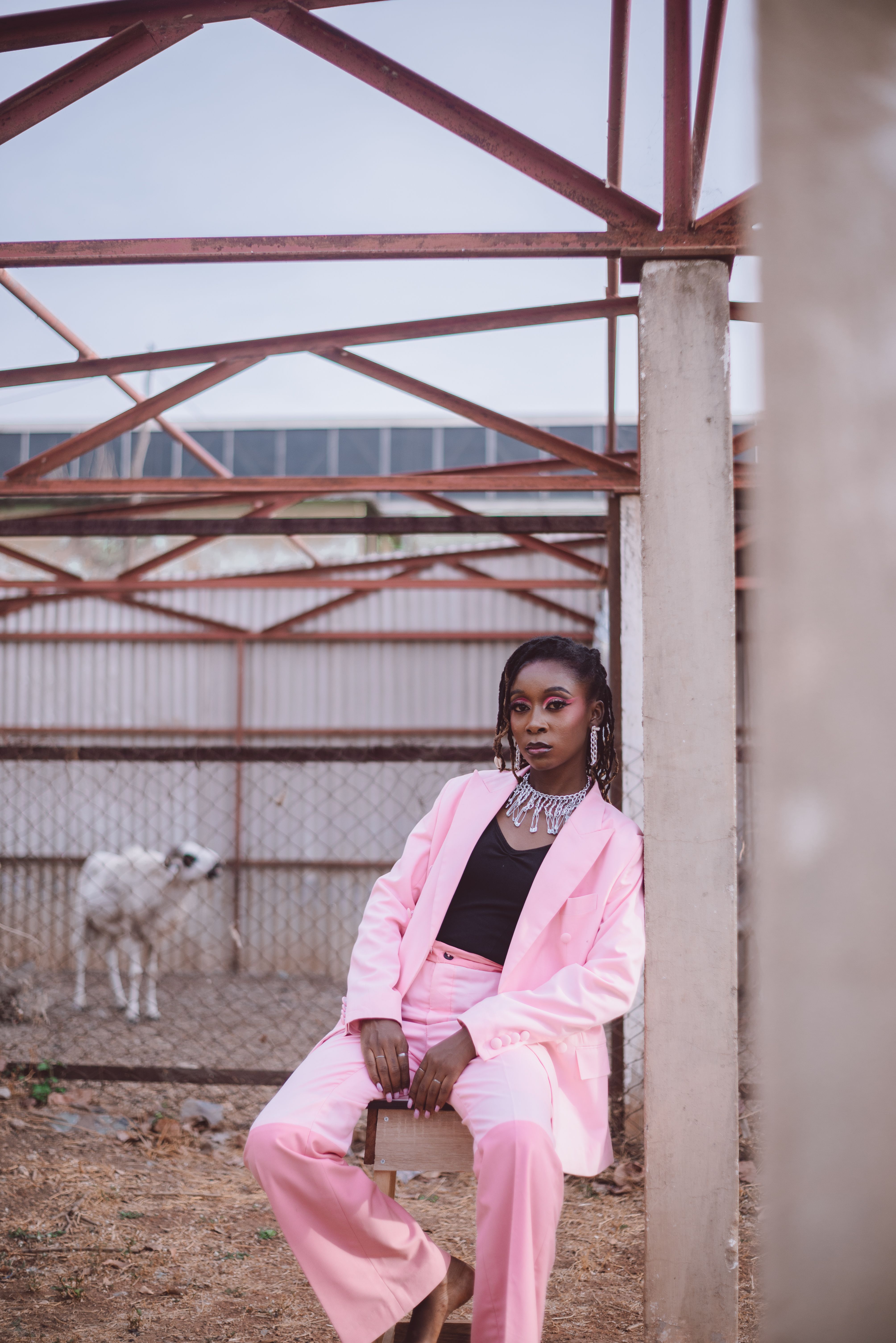 Stylish woman in pink suit, posing outdoors with a dog in a rustic setting.