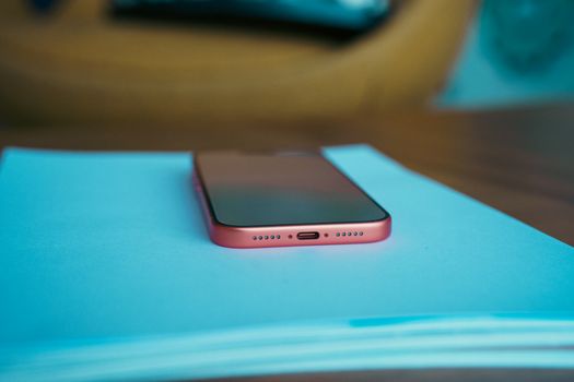 Close-up of a pink smartphone resting on blue paper against a blurred wooden background, highlighting sleek design.