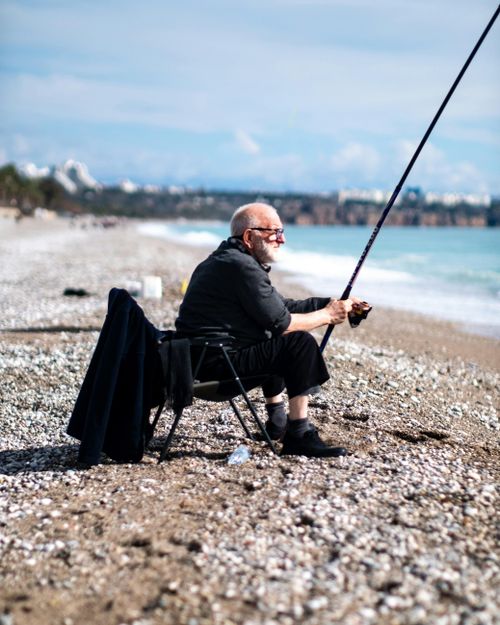 Free Senior man enjoying a day of fishing on a picturesque pebble beach with a distant coastline view. Stock Photo