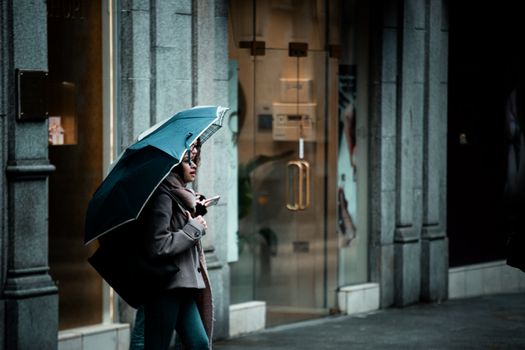 A woman walks with an umbrella near a shopfront on a rainy day in Ireland, capturing urban life.