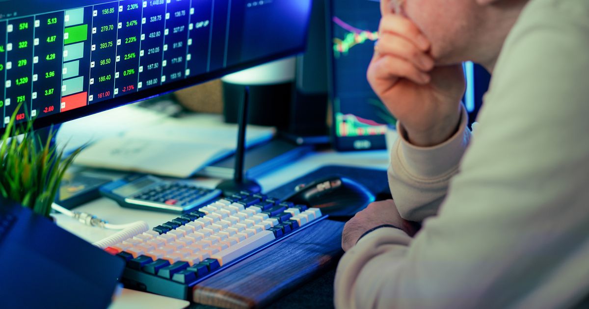A stock trader studies financial market data across several screens.