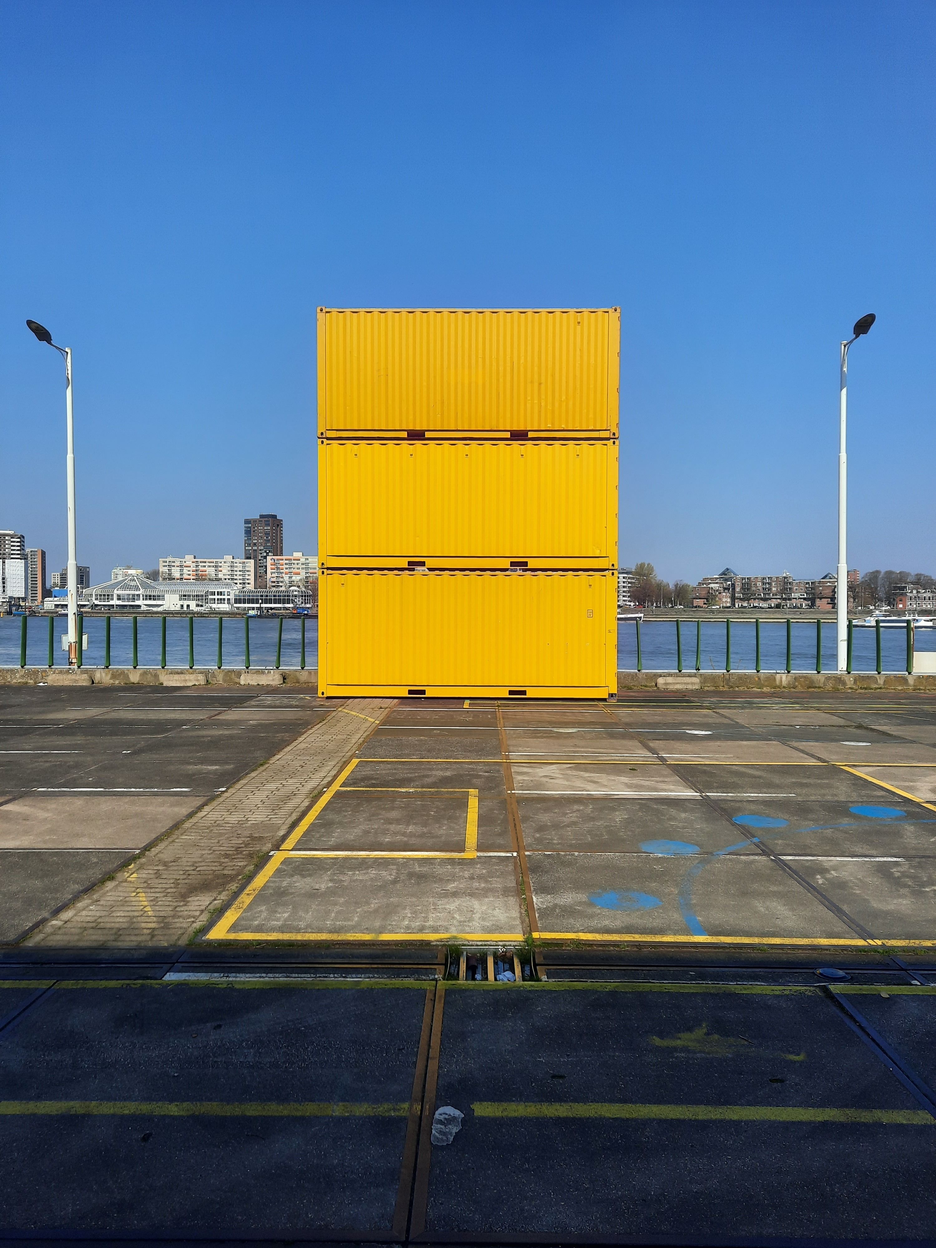 Stack of yellow shipping containers by a harbor in Rotterdam, with a clear blue sky.