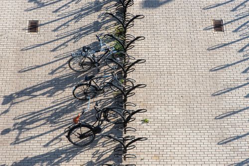 Free A top-down view of a bicycle stand casting long shadows on a sunny paved area. Stock Photo