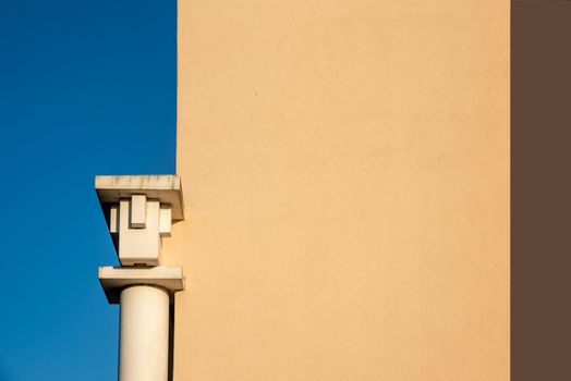 Minimalist architectural detail featuring a modern pillar juxtaposed with a beige facade against a clear blue sky.