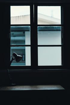 A moody interior scene featuring a window and desk lamp, casting a subtle silhouette.
