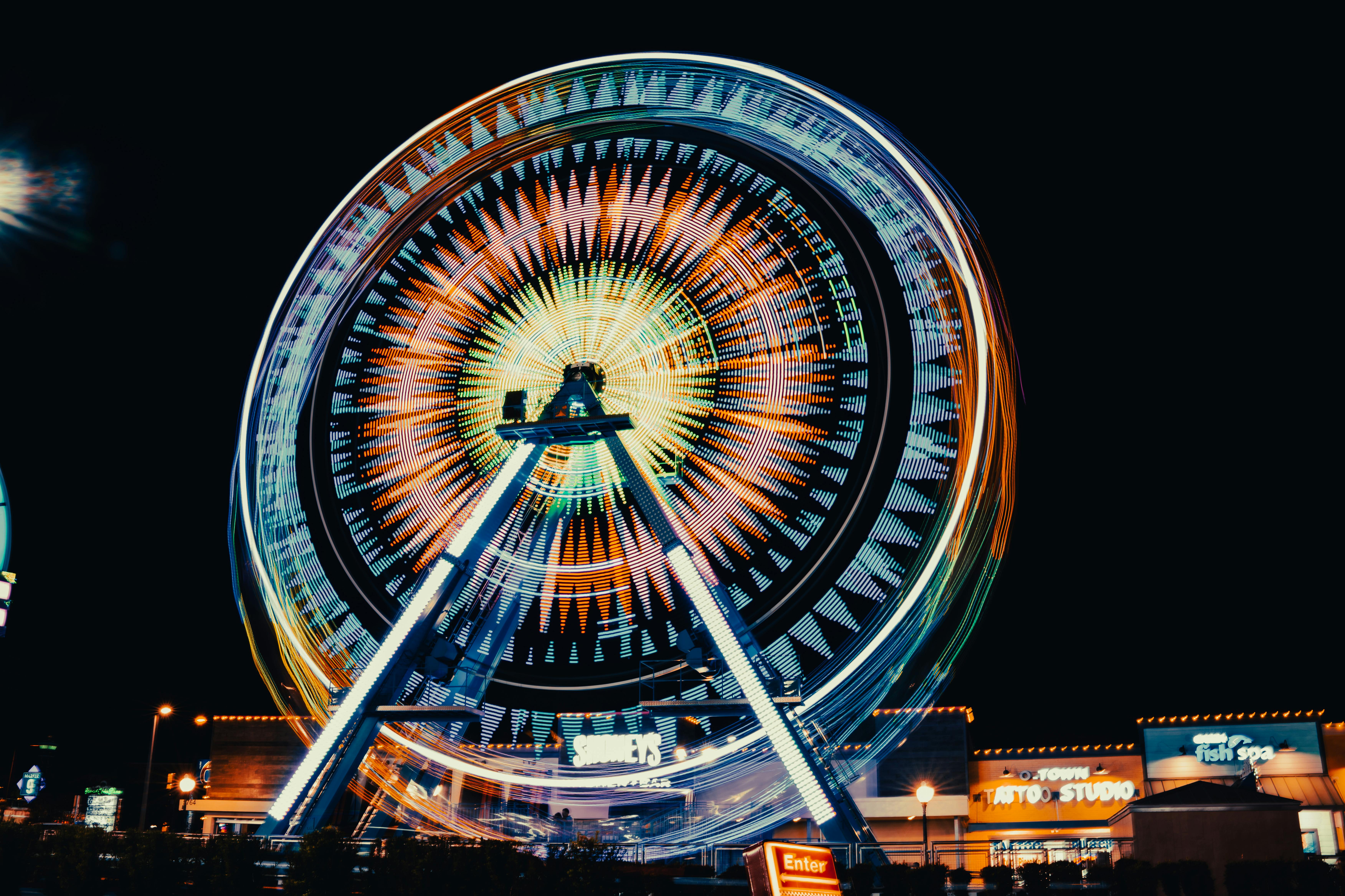 Colorful long exposure of a Ferris wheel at night, capturing vibrant light trails in an amusement park setting.