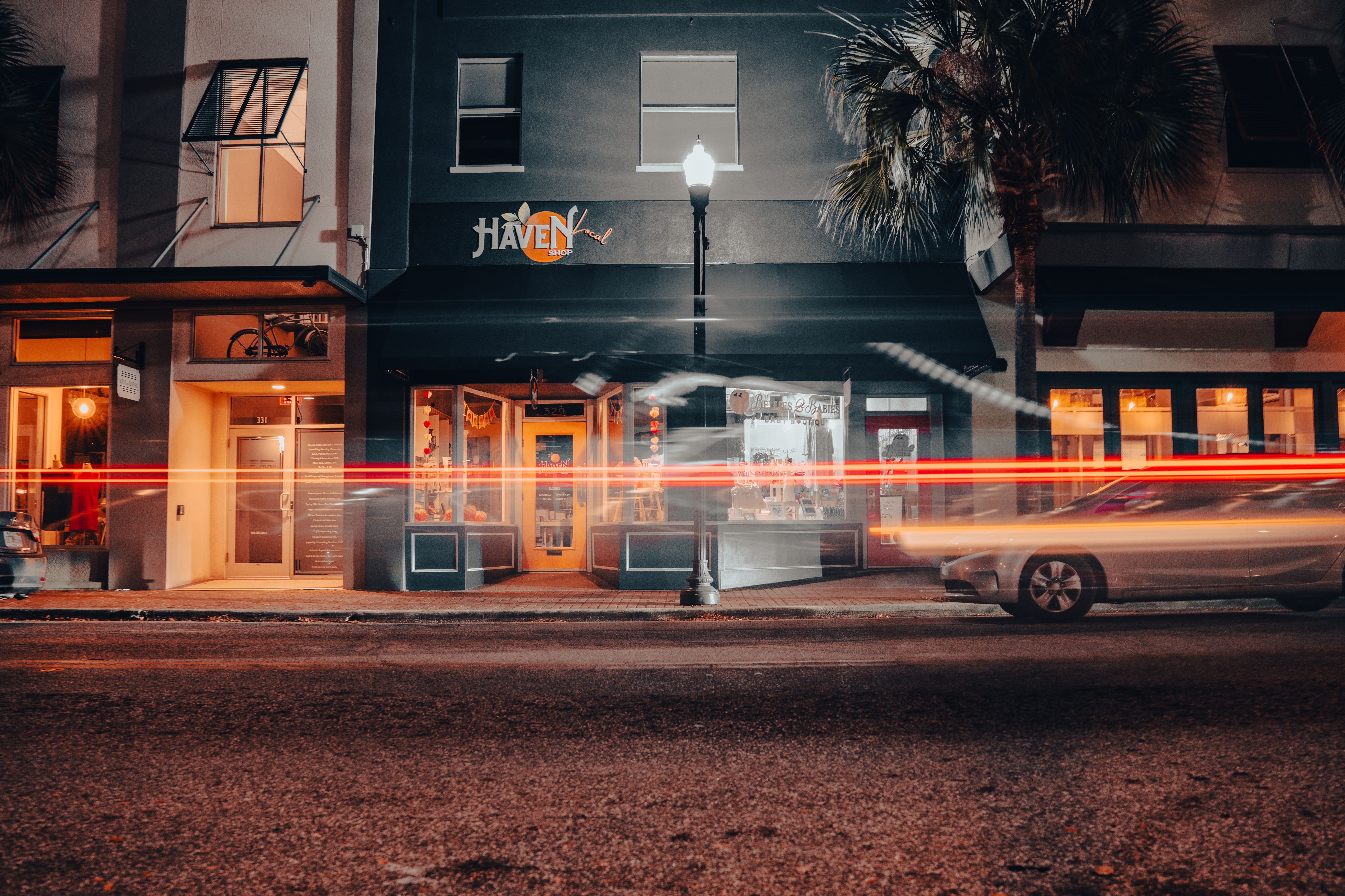 A vibrant street scene at night showcasing motion blur light trails in front of a storefront.